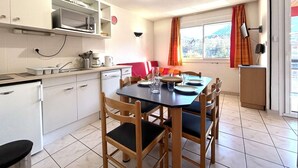 A compact kitchen with a dining area, white cabinets, a microwave, and a window with curtains.