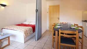 A compact room with a bed, a dining table with chairs, a small kitchen area, and a door.