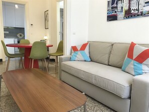 A living room with a sofa, a wooden coffee table, and a dining area with a red table and green chairs.