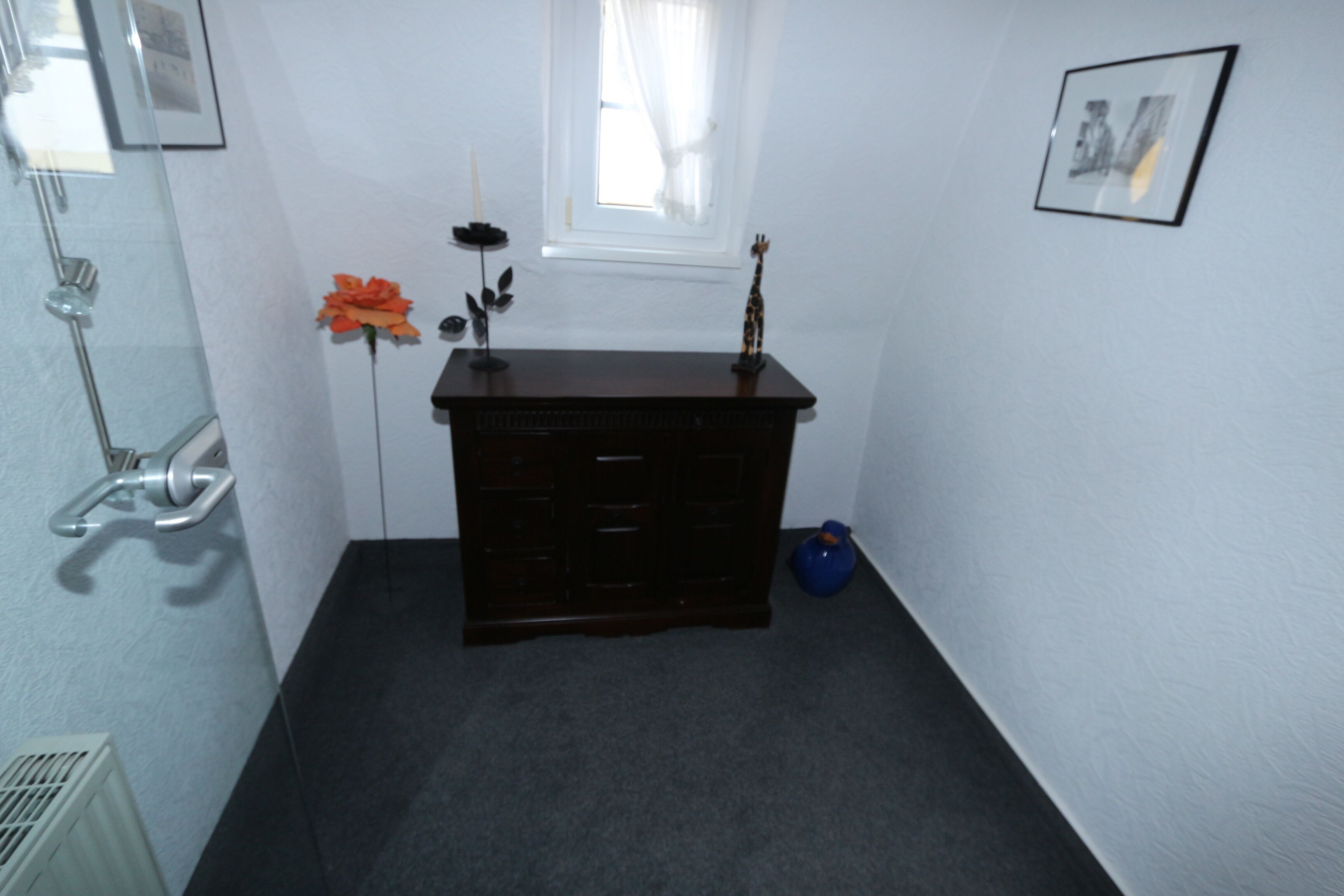 A small, dark wooden dresser with drawers, a small blue vase, and a framed picture on the wall.