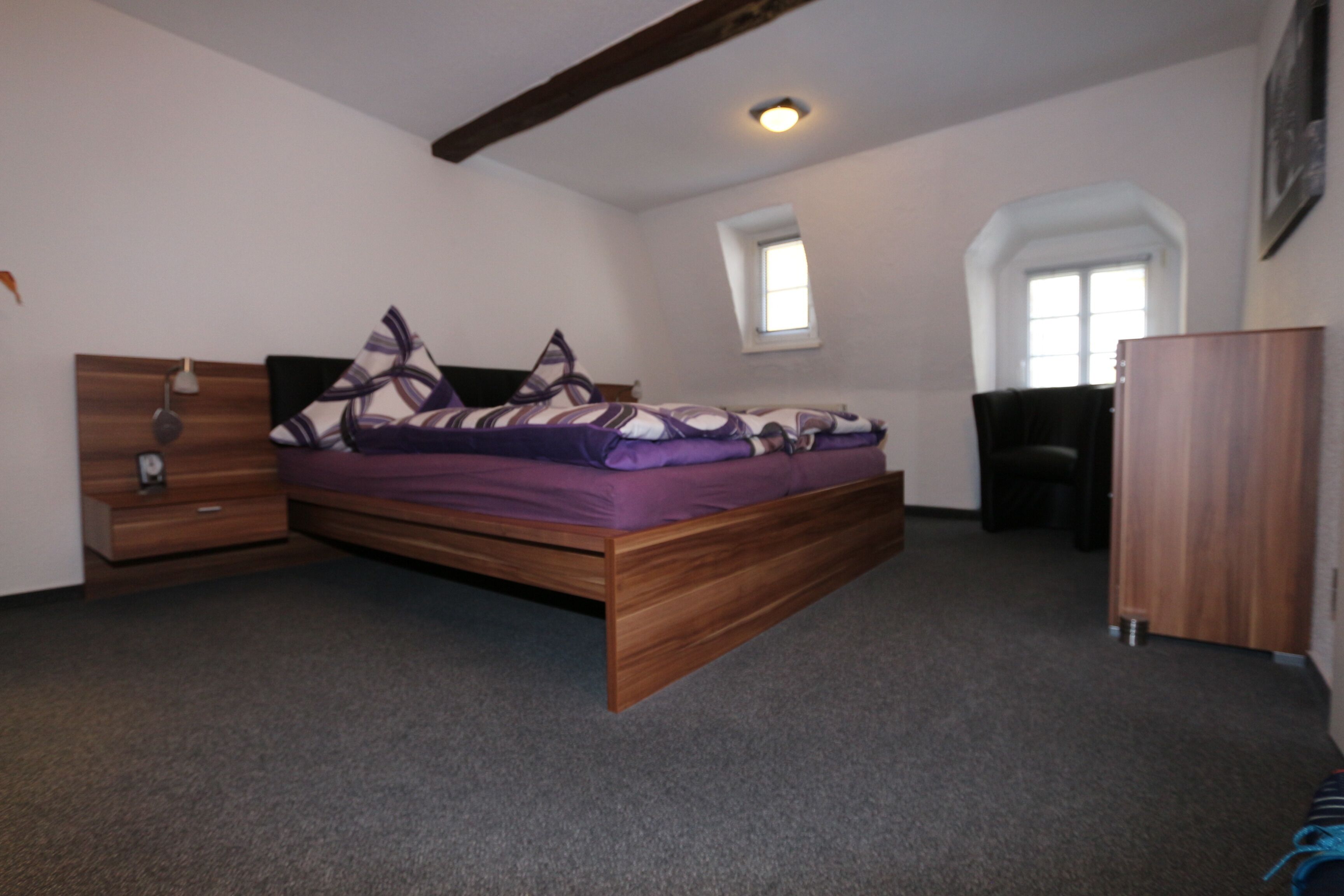 A bedroom with a wooden bed, a nightstand, a dresser, and a window with a view of the outside.