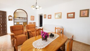 Zona pranzo con tavolo in legno, sedie e lampadario. Alle pareti sono presenti quadri incorniciati e, sullo sfondo, una cucina.