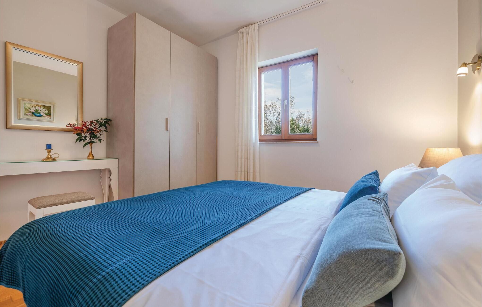 A bedroom with a bed, a window, a bedside table with a lamp, and a mirror.