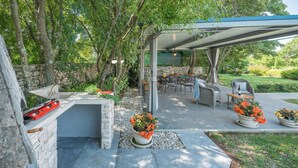 Terrassa exterior amb una barbacoa de pedra, zona de seients i plantes en testos.