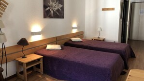 Habitación de hotel con dos camas, una mesita de noche, una lámpara, un cuadro y una puerta que da al baño.