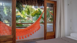 Una habitación con una cama, una hamaca y vistas a plantas tropicales a través de una puerta de cristal.