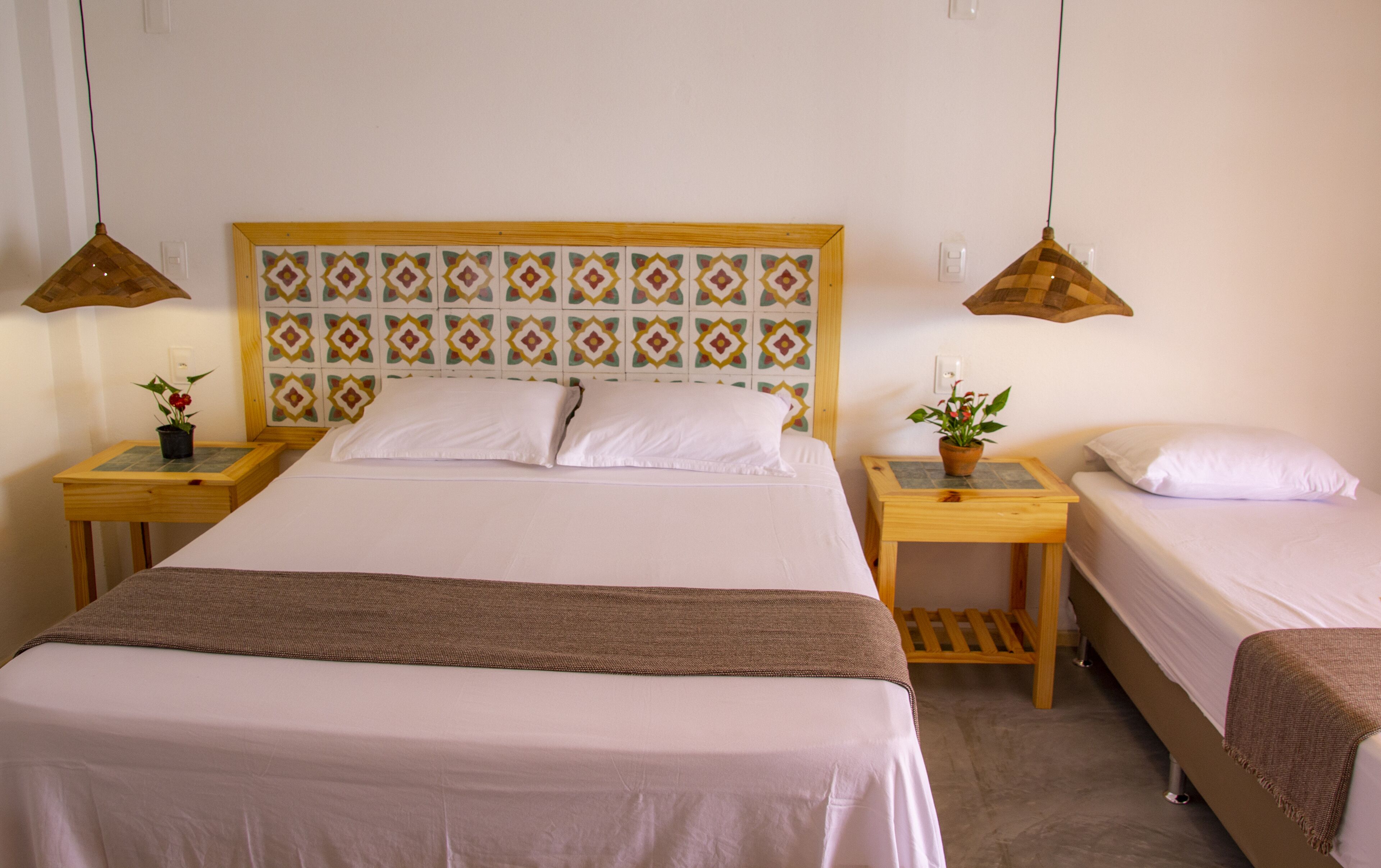 Una habitación de hotel con una cama grande, dos mesitas de noche y dos lámparas colgantes.
