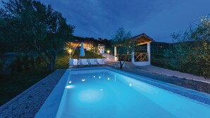 Ein Pool mit Liegestühlen und einer überdachten Sitzgelegenheit im Abendlicht.