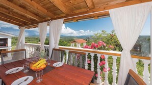 Eine Holzterrasse mit gedecktem Tisch für zwei Personen, mit Blick auf eine malerische Landschaft mit Bergen und einem kleinen Gebäude.