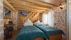 Ein gemütliches Zimmer mit zwei Betten, Holzbalken, Steinwänden und einem großen Fenster.