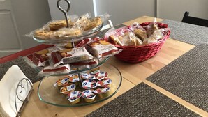 Une table sur laquelle se trouve un présentoir en verre contenant des pâtisseries, un panier rouge rempli de pain et un saladier en verre contenant des en-cas emballés.