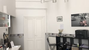 Une pièce avec une porte blanche, un radiateur, un bureau avec une imprimante Canon, une chaise et une étagère contenant divers objets.