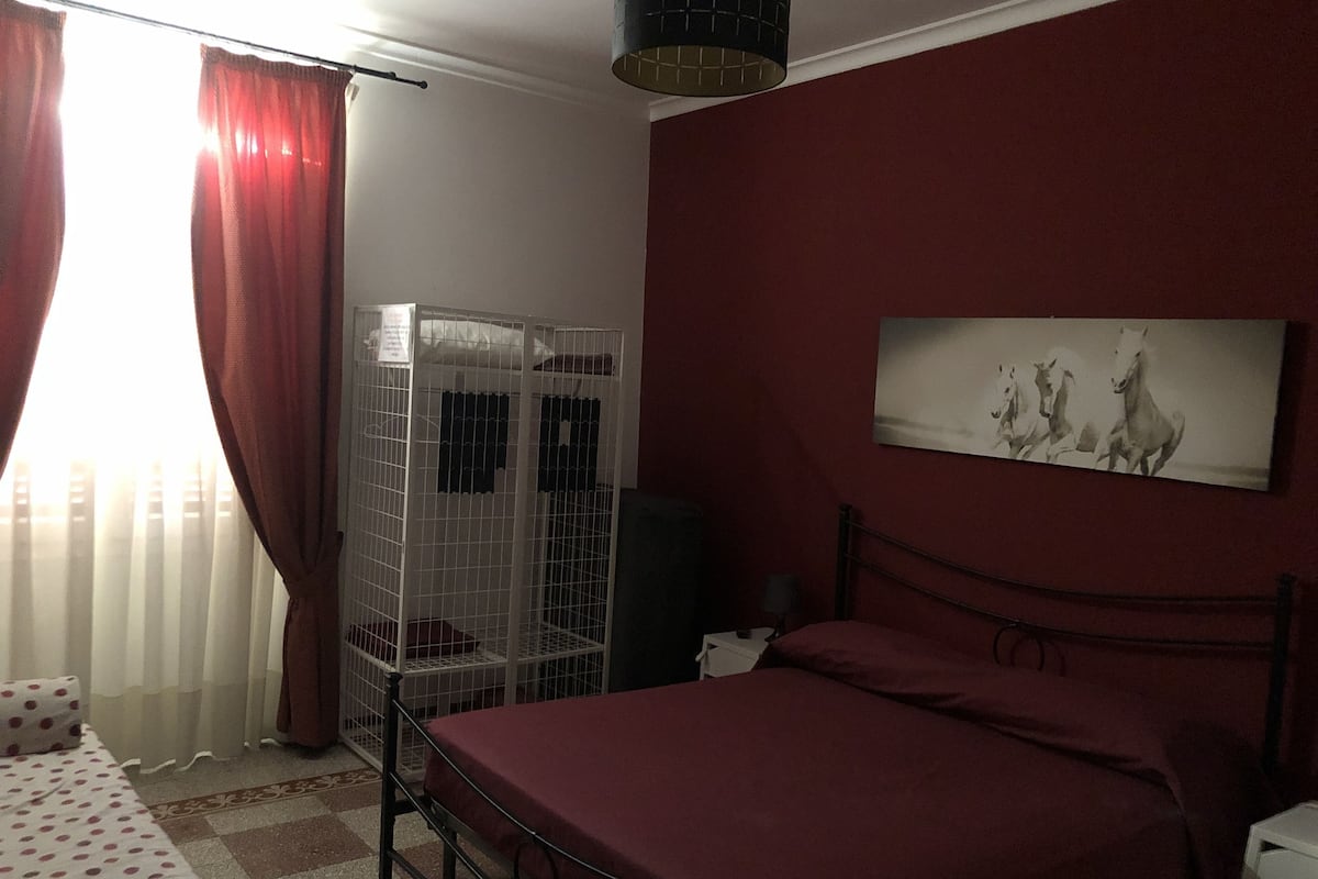 A bedroom with a bed, a wardrobe, a chair, a lamp, and a painting on the wall.