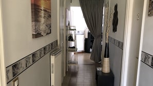 Un couloir avec un sol carrelé, un radiateur, une étagère avec des objets et une porte avec un rideau.