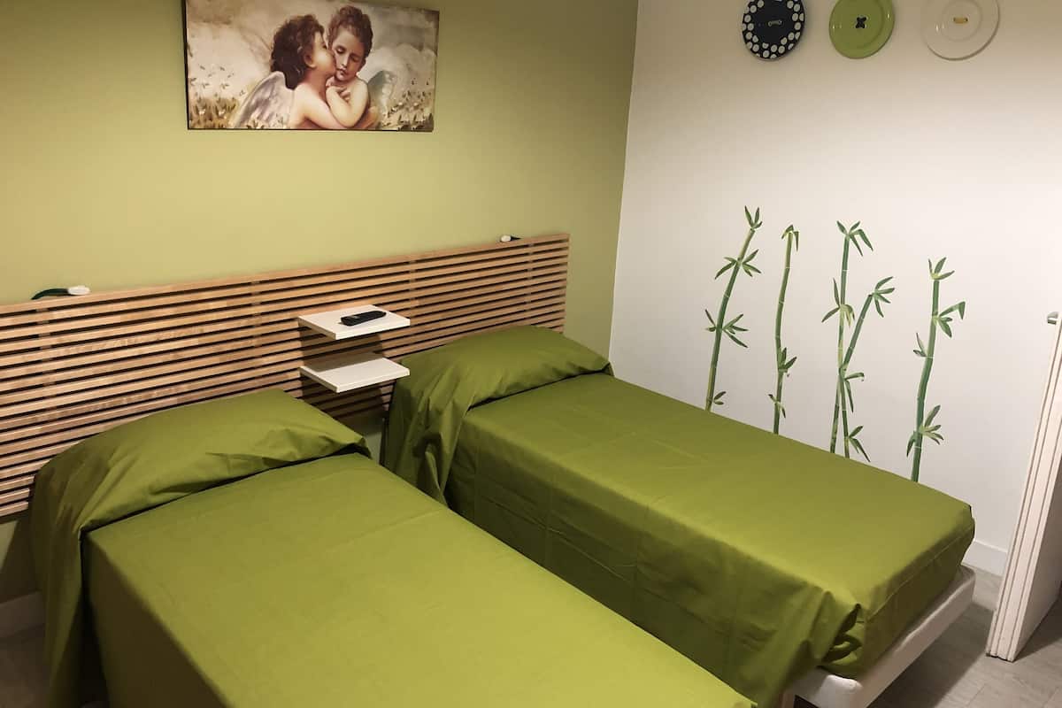 A room with two beds, a wooden headboard, a painting of cherubs, and a wall with bamboo illustrations.