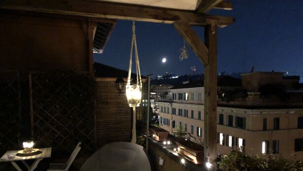 Un balcon avec une suspension lumineuse, une chaise blanche et une petite table.