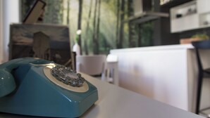 Sinivihreä pyörivä puhelin valkoisella pöydällä huoneessa, jossa on suuri ikkuna, josta avautuu näkymä metsään.