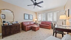 A living room with a brown leather sofa, a glass coffee table, a wooden sideboard, a ceiling fan, and a window with blinds. - Availability 11/30/19 to 12/7/19  (Beaver Creek)