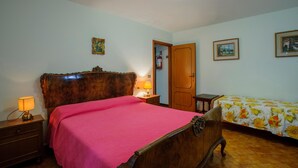 A bedroom with a wooden bed, a bedside table with a lamp, a door, and a small table with a floral tablecloth. - Nice apartment in Misano Adriatico (RN) (Misano Adriatico (RN))