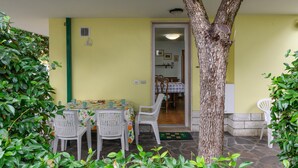 A dining area with a table set for four, surrounded by chairs. A tree trunk is visible in the foreground, and a door leads to another room. - Nice apartment in Misano Adriatico (RN) (Misano Adriatico (RN))