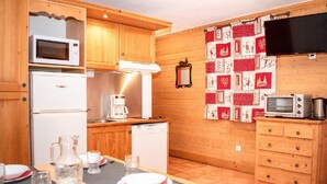 Una cocina compacta con armarios de madera, un microondas, una cafetera y un refrigerador pequeño.