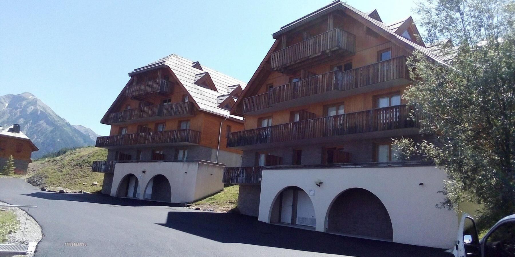 A row of wooden multi-story buildings with balconies, set against a mountainous backdrop.