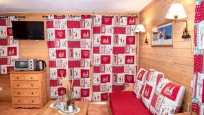 Una habitación acogedora con una cama de madera, una mesita con un florero, un microondas y un televisor en la pared.
