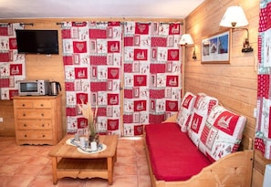A cozy room with a wooden bed, a small table with a vase, a microwave, and a TV mounted on the wall.