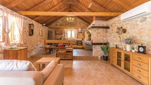 A rustic interior with a stone wall, wooden beams, a stone fireplace, a kitchen area, and a seating area with a sofa and a table. - Cozy home in Jagodnja Gornja (Jagodnja Gornja)
