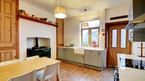 A kitchen with wooden cabinets, a dining table with chairs, a stove, and a window with a view of greenery. - Victorian townhouse near International Conference Centre / Kings Quarter (Harrogate)