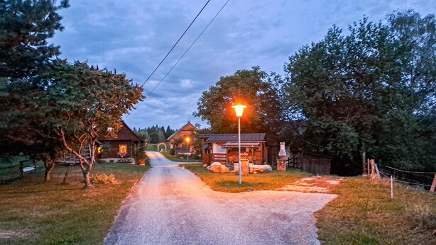 A rural road leading to a row of wooden cabins with a street lamp in the center. - Ferienhaus mit Fernblick (Deutschlandsberg)