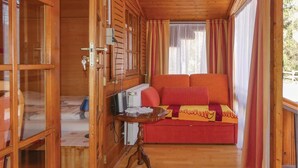 A cozy room with a wooden interior, a bed with red and yellow bedding, a small table with a lamp, and a window with curtains. - Ferienhaus mit Fernblick (Deutschlandsberg)