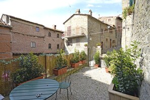 Un cortile con tavolo e sedie, circondato da edifici in pietra e piante in vaso.