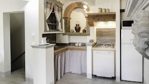 Una cocina compacta con estufa a gas, horno empotrado y refrigerador. Hay un estante de madera sobre la estufa y una ventana pequeña con cortinas.