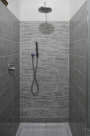 Una doccia con soffione a pioggia e doccetta, in un bagno piastrellato con parete strutturata.