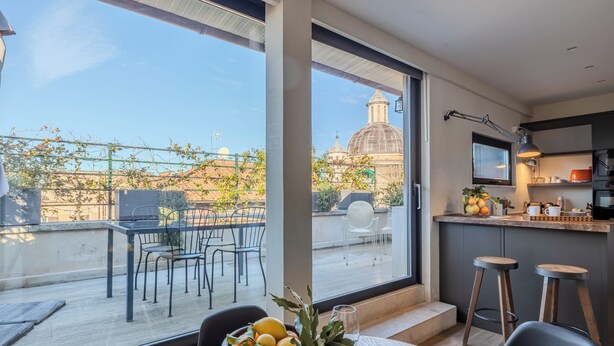 A modern kitchen with a large window, a dining area with a table set for two, and a view of a historic building. - Romantic Terrace Hideaway in the Heart of Rome (Roma)