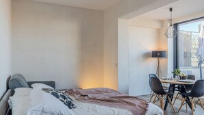 A modern bedroom with a large bed, a dining table with chairs, and a view of the outside through a large window. - Romantic Terrace Hideaway in the Heart of Rome (Roma)