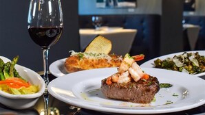 A dining table with plates of food, a glass of red wine, and a decorative wall in the background. - Hotel Legends (Biloxi)