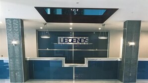 A hotel reception area with a modern design, featuring a reception desk, a glass partition, and a patterned floor. - Hotel Legends (Biloxi)