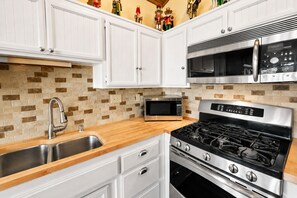 A modern kitchen with white cabinets, a stainless steel microwave, a gas stove, and a sink.