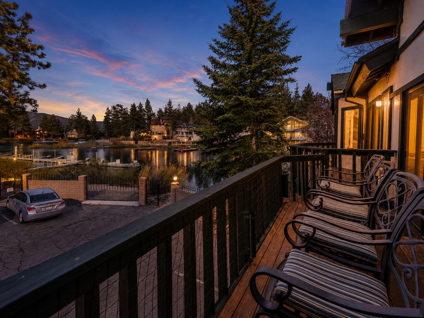 A waterfront property with a wooden deck, outdoor seating, and a view of a lake and surrounding houses.