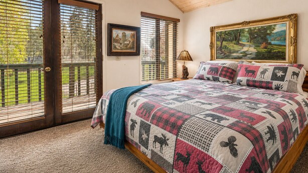 A bedroom with a large bed, a painting, and a window with blinds. - Lakefront Viking Oasis Condo - Lakefront, Indoor Pool, Hot Tub (Big Bear Lake)