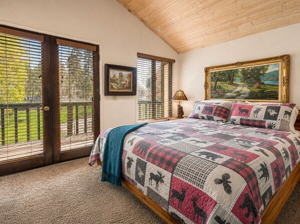 A bedroom with a large bed, a painting, and a window with blinds.