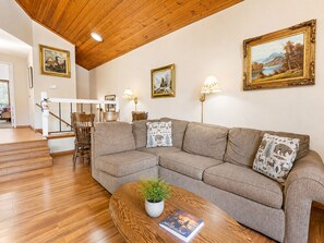 Ein Wohnzimmer mit Holzboden, einer Couch, einem Couchtisch mit Pflanze und gerahmten Bildern an den Wänden.