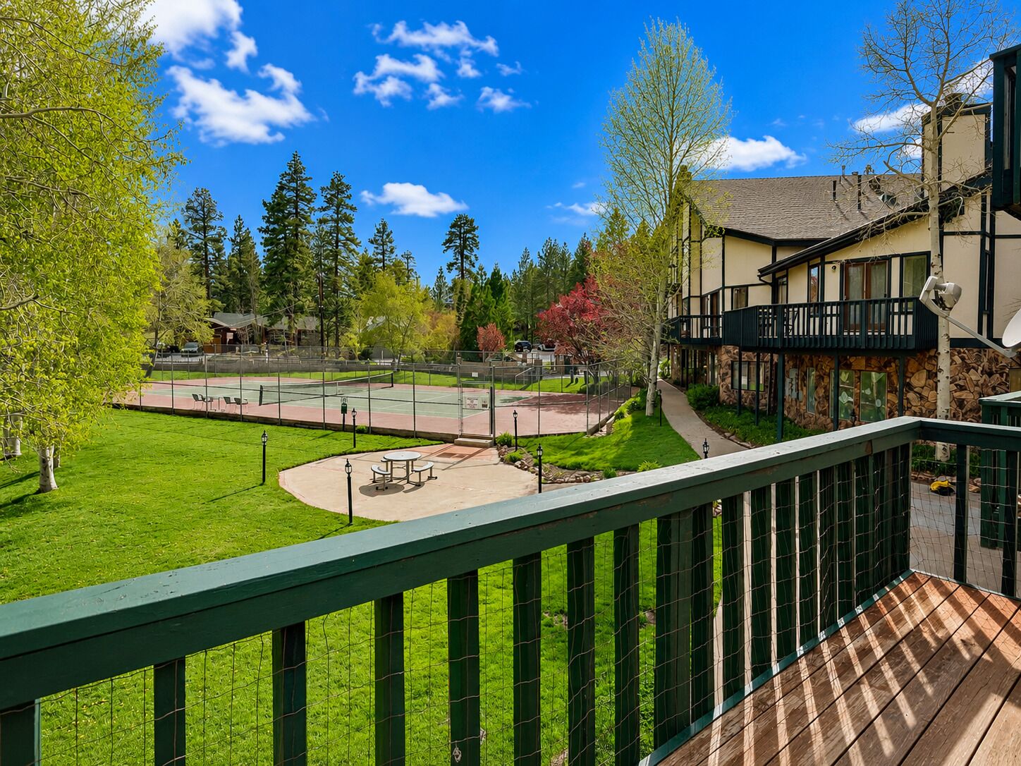 A residential area with a tennis court, a wooden deck, and a building with a balcony.