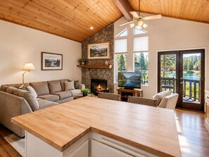 A spacious living area with a stone fireplace, a large wooden dining table, and a view of a lake through glass doors.