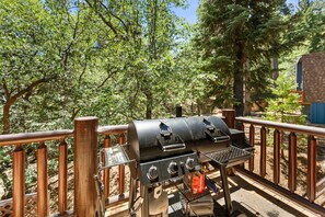 Una parrilla para barbacoa en una terraza de madera con vista a los árboles.