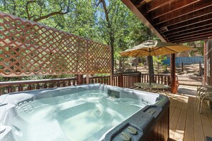 Een hottub op een houten terras, met een houten schutting, een tafel en een parasol.