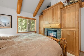 A bedroom with a bed, a fireplace, wooden beams, and a window with blinds.