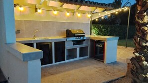 An outdoor kitchen with a grill, sink, and storage cabinets, surrounded by a pergola with string lights. - Romantic finca with pool between Campos and Colonia Sant Jordi in the countryside (Campos)